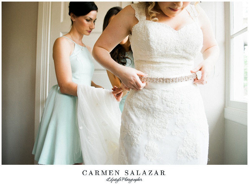bridesmaids help a bride get dressed in natural light